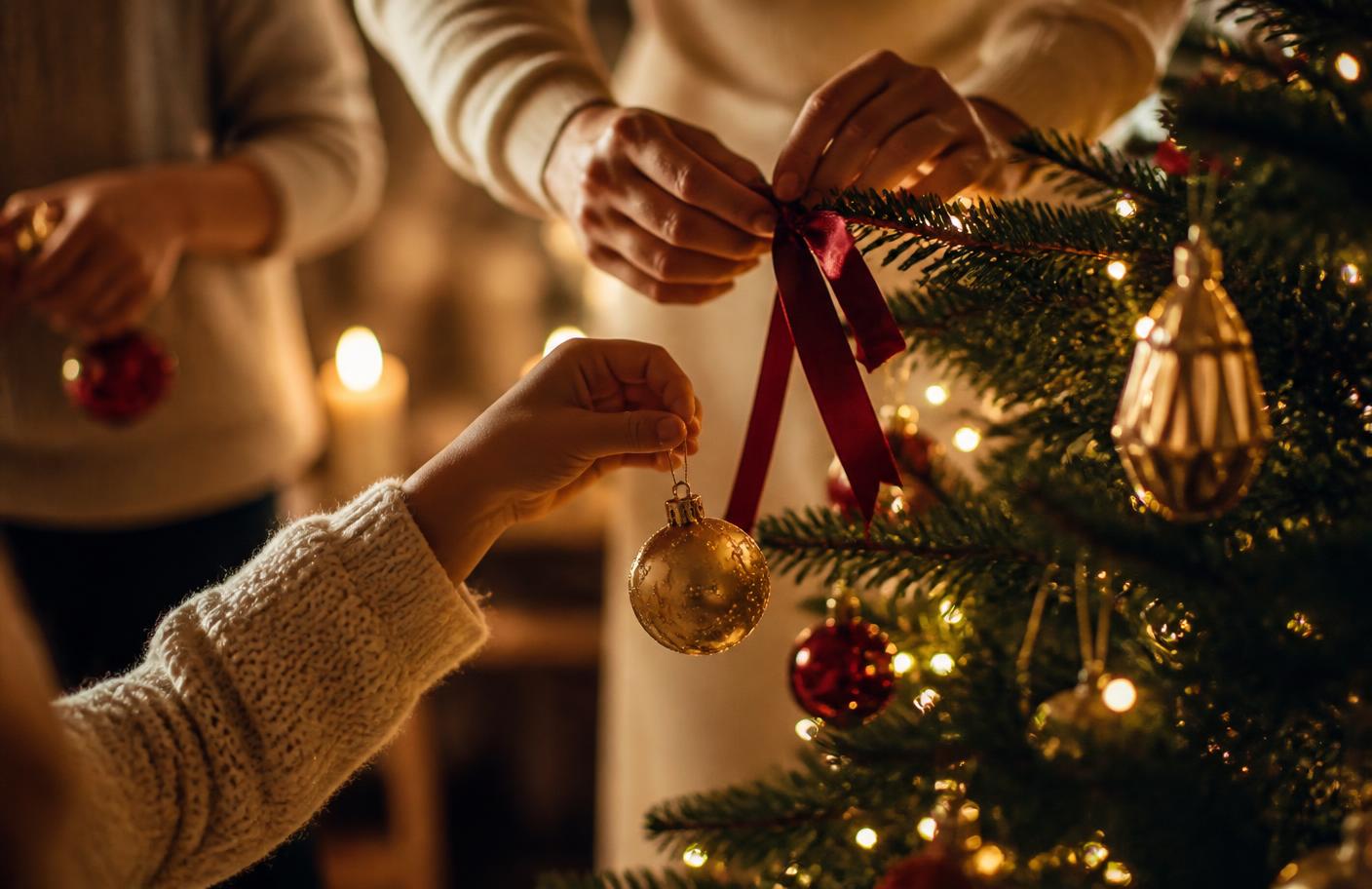 Mains décorant une branche de sapin avec un ornement doré